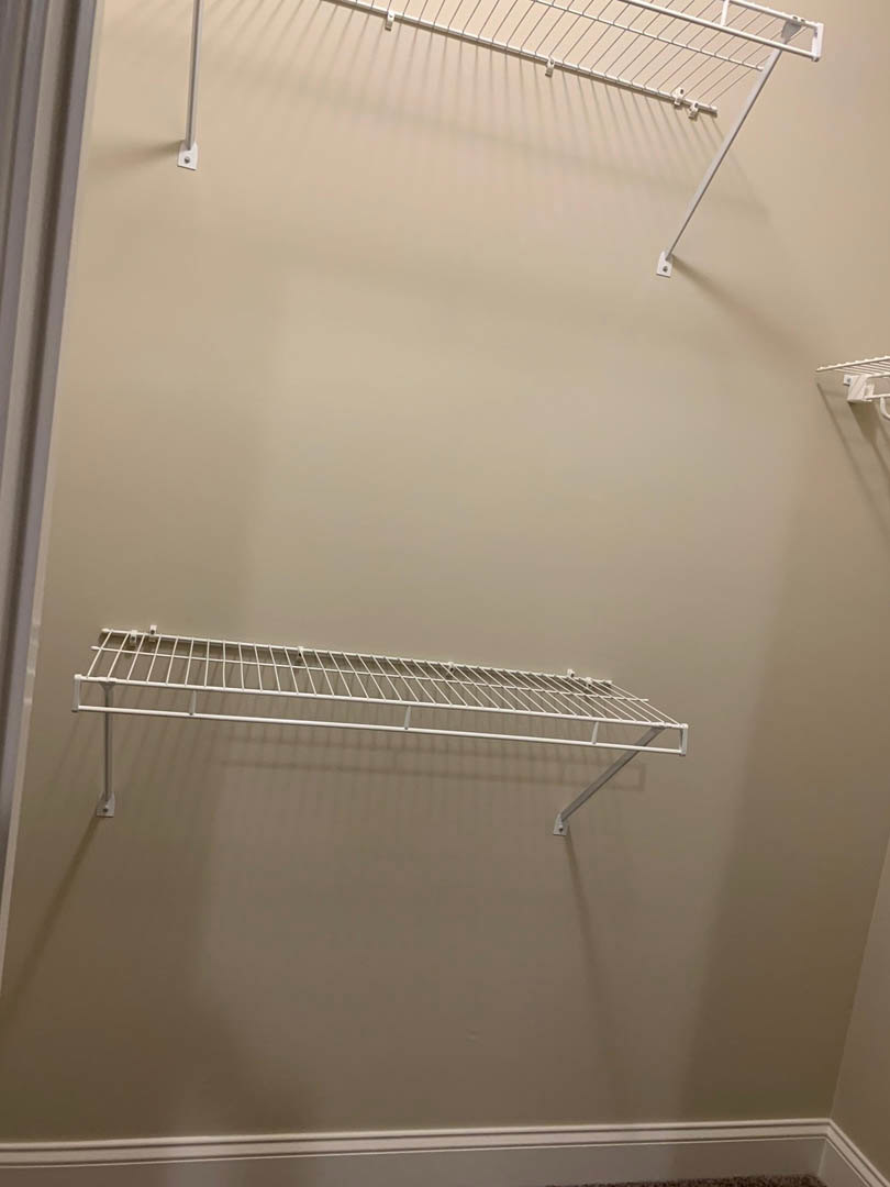 White wire shelf mounted on a white wall above white molding, adjacent to a white door and handle, in a bathroom interior.