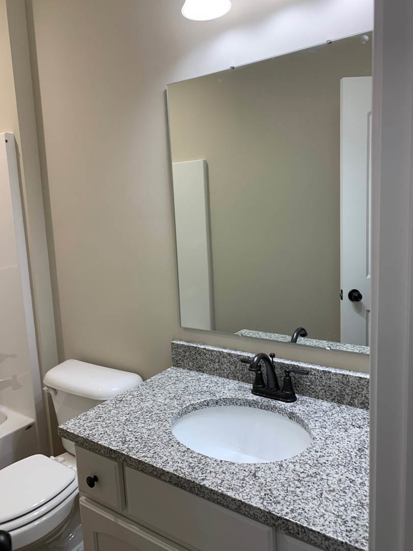 White porcelain sink with black border and matte black faucet, adjacent to a modern toilet; white door with mirrored panel, light gray tiled walls, and minimal bathroom