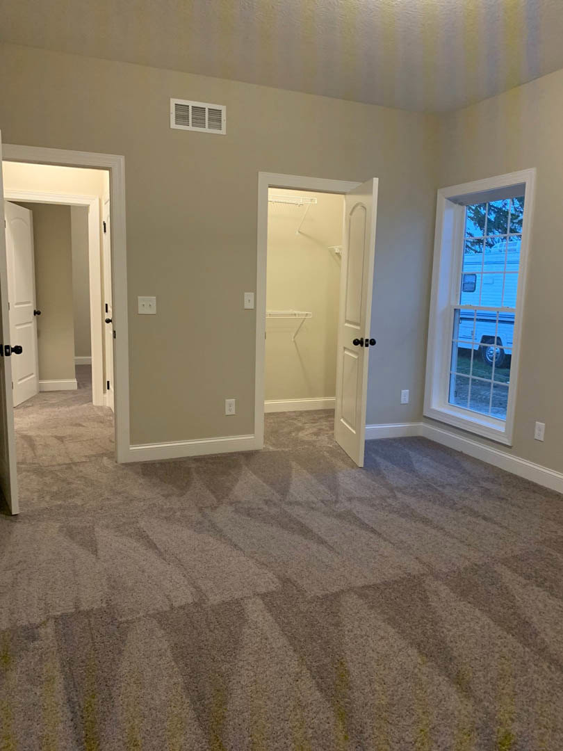 Carpeted room with white walls, two white doors with black knobs, window overlooking a trailer, wall vent, and closet with white door