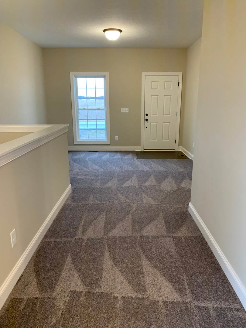 Carpeted hallway with white door featuring black knobs, window overlooking ocean, wall and ceiling light fixtures