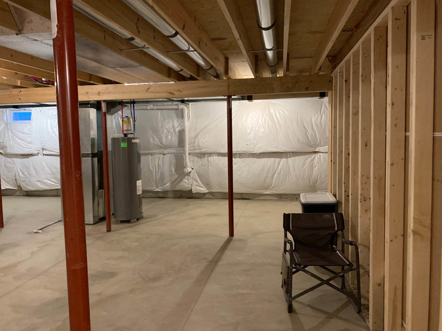 Small room with folding chair, water cooler, white sink with black base, red metal pole, white plastic wall covering, and close-up of door.