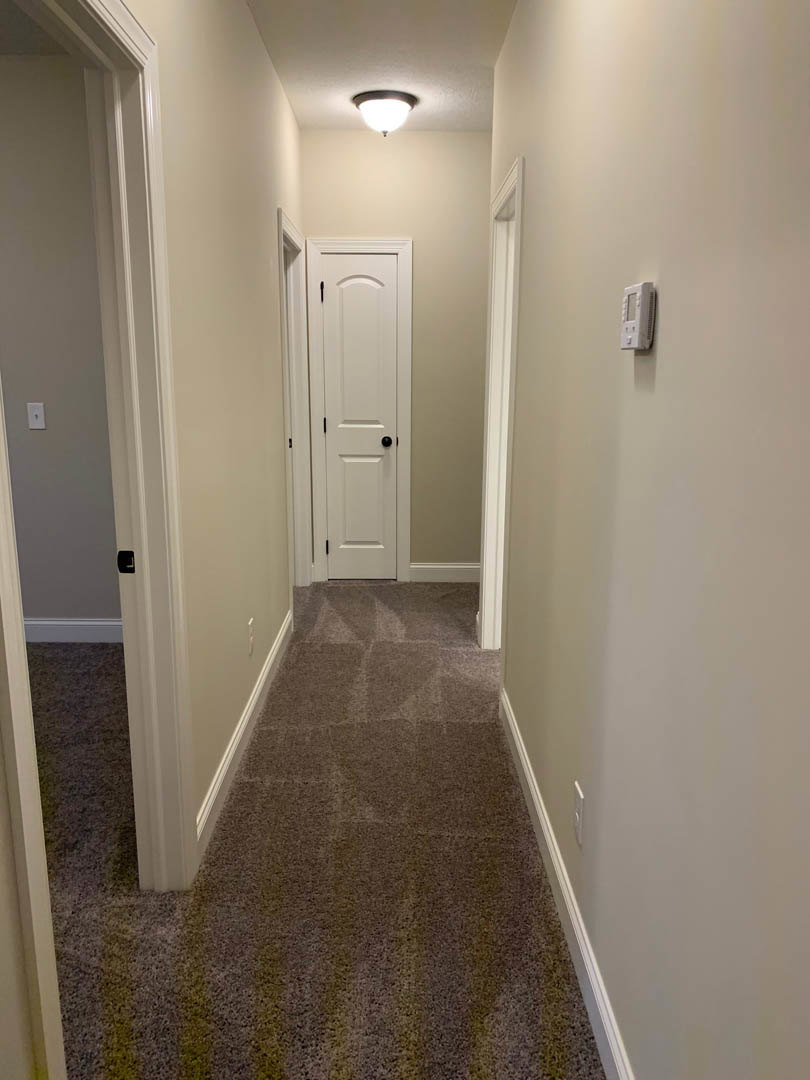 Hallway with carpeted walls, white door with black knob, ceiling-mounted light fixture, tile flooring, and white plaster walls