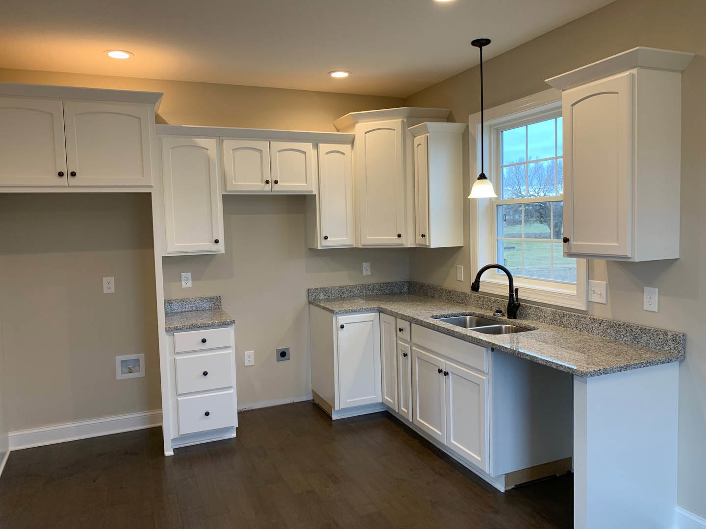 White kitchen cabinets with black knobs, granite countertops, black faucet, black ceiling pole, white doors, and drawers.
