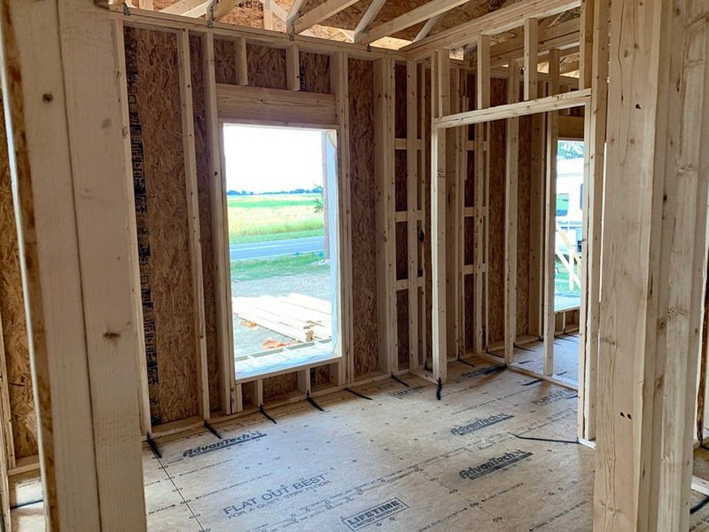 Sunlit room featuring a large window with a view of the road, wood plank flooring, white walls, and a wooden door.