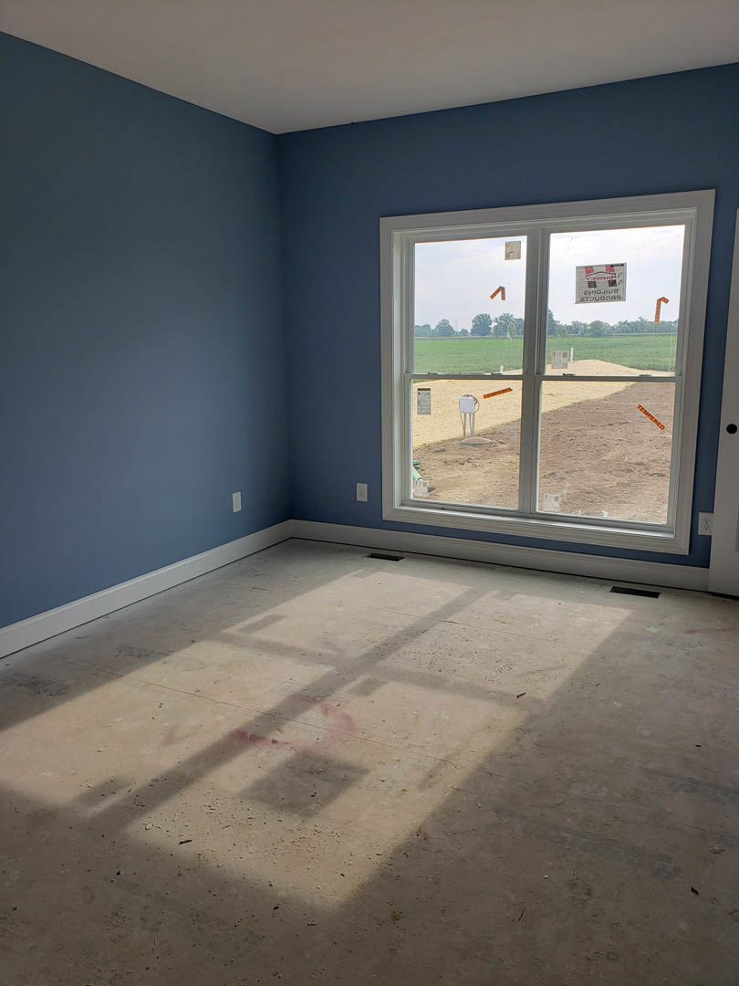 Sunlit room with plaster walls, composite flooring, large window overlooking grassy field, shadow cast across floor.