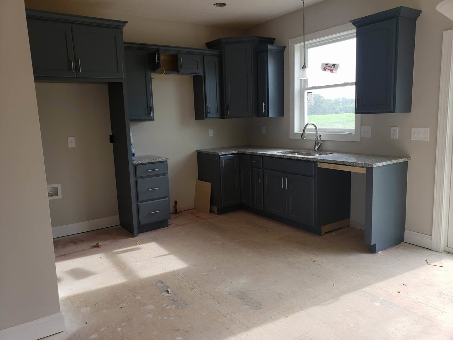 Modern kitchen featuring white cabinets, stainless steel sink with chrome faucet, black lower cabinetry, light stone countertop, large window, and hardwood flooring.
