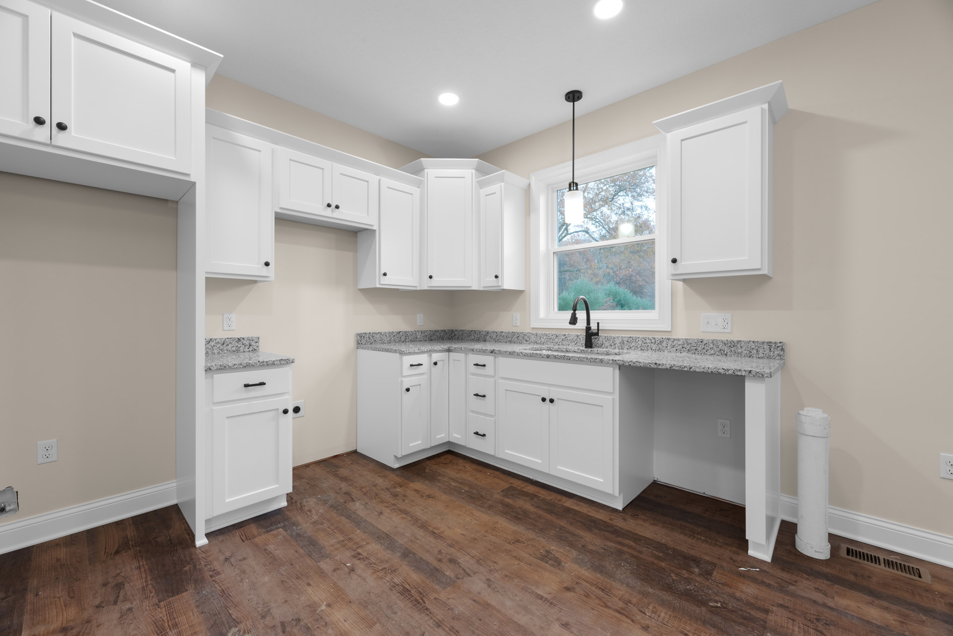 Kitchen with white shaker cabinets, granite countertops, wood flooring, black faucet, and stainless steel sink