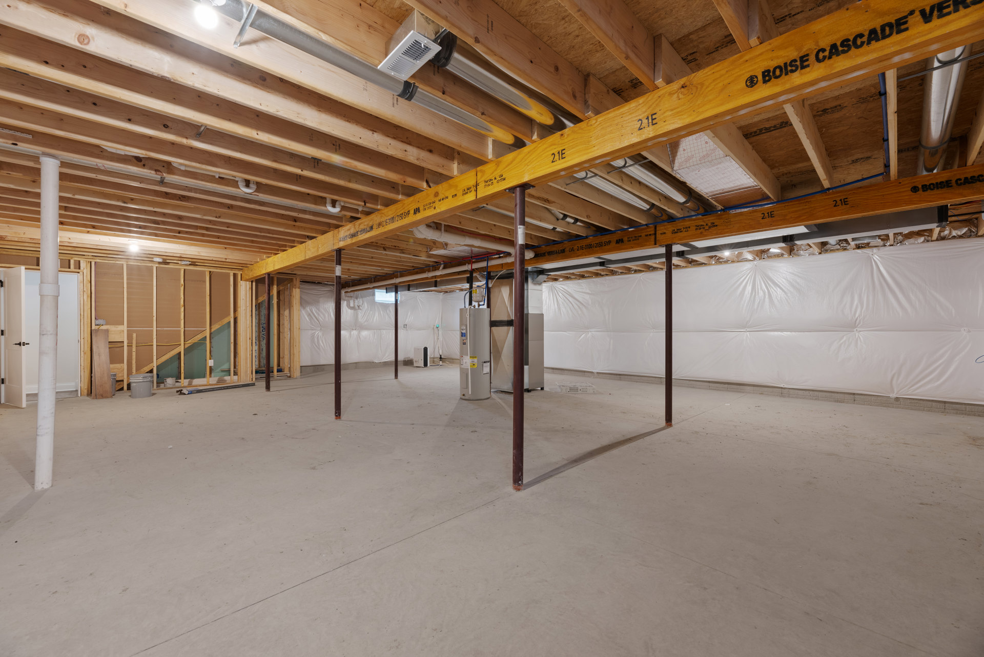 Exposed wood beam and steel beam in ceiling, concrete floor with metal support pole, white vent on wood surface, visible pipes in unfinished wood ceiling