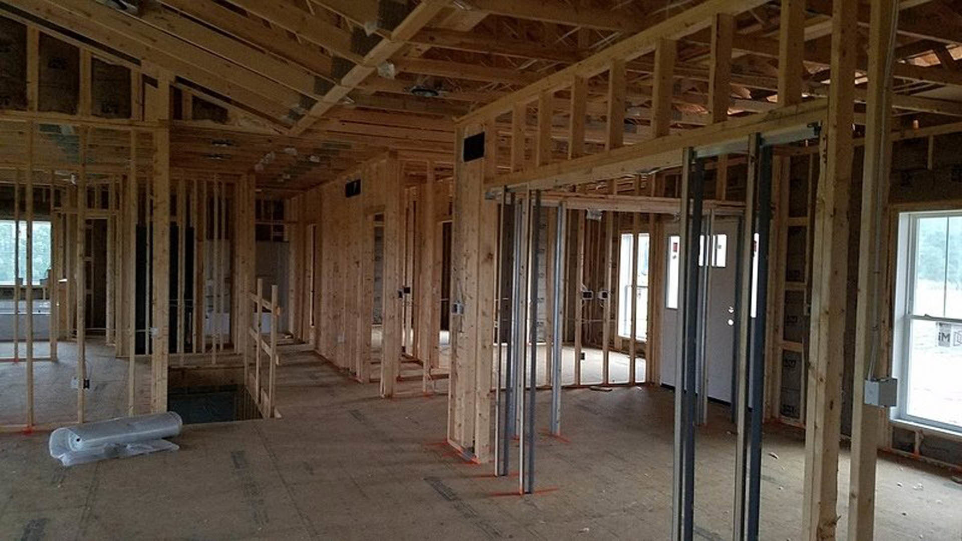 Living room with exposed wood ceiling beams, light hardwood floors, large window, and a wooden door