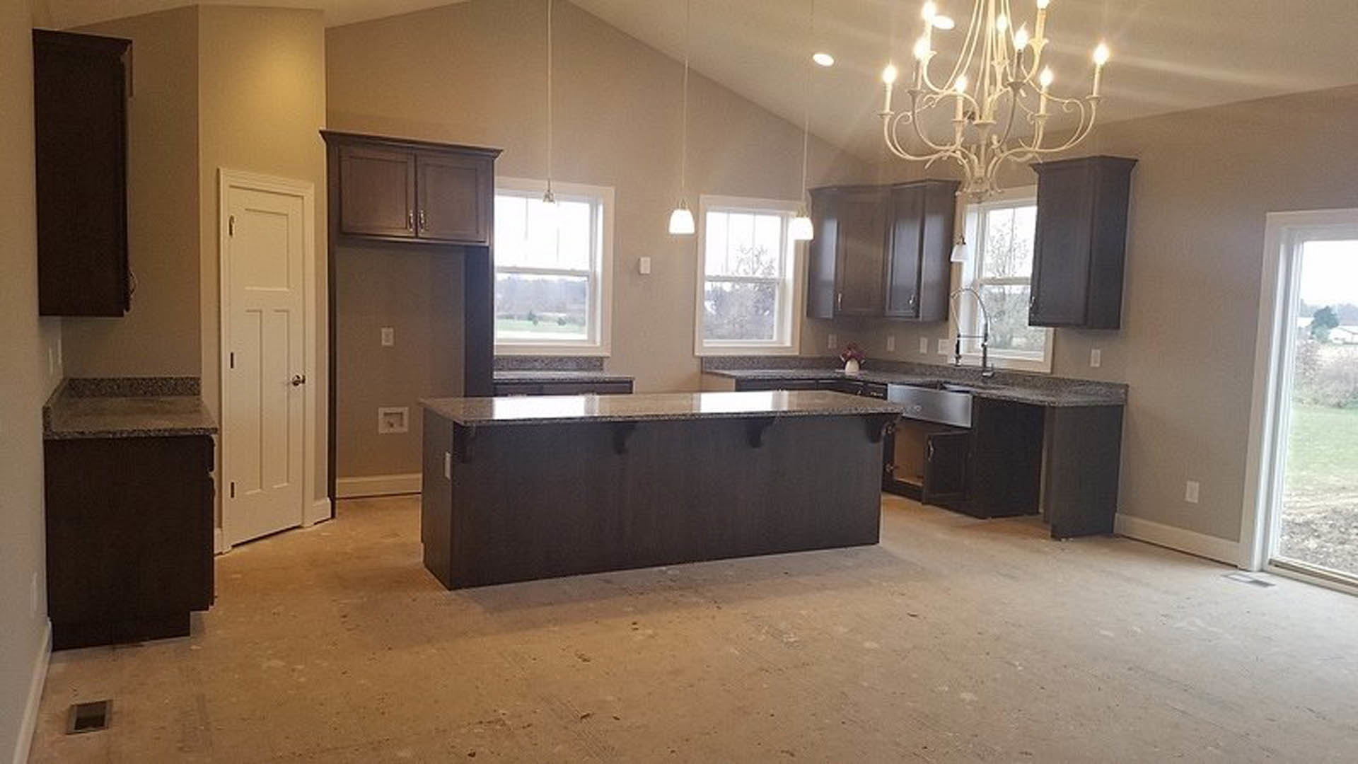 Modern kitchen featuring a black island with white countertop, elegant chandelier lighting, white cabinetry with silver handles, and a window overlooking a green lawn.