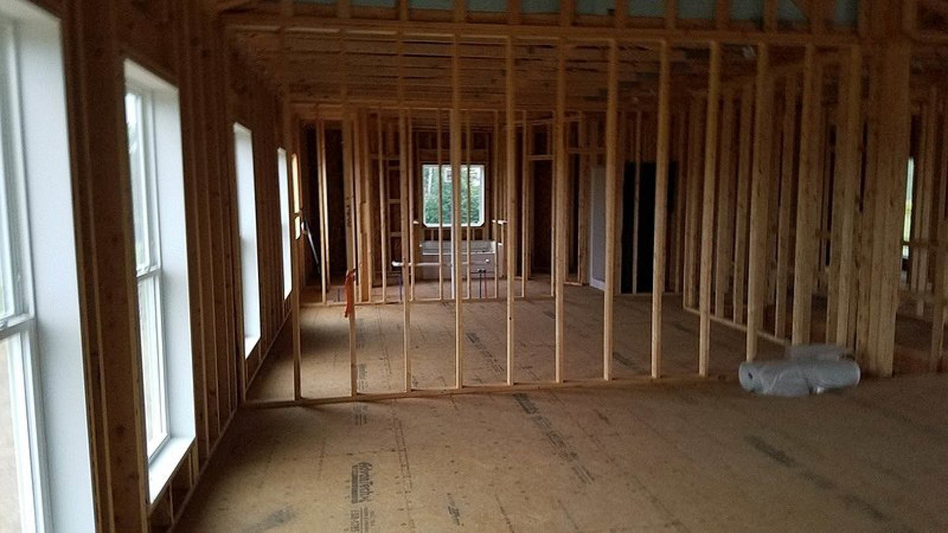 Room under construction with exposed wood framing, ceiling beams, and a window letting in natural light