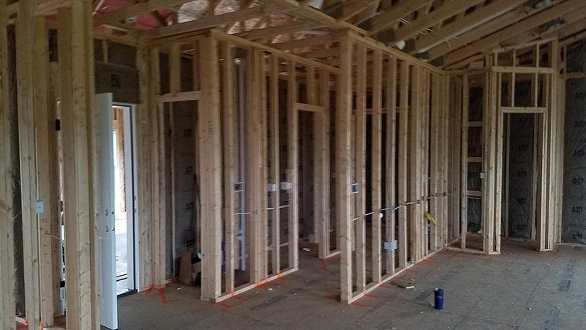 Exposed wooden beams and framing inside a partially constructed house, with insulation visible between planks and unfinished ceiling