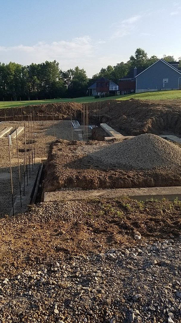 Gravel and dirt pile beside house with basketball hoop, trees, and blue sky in background