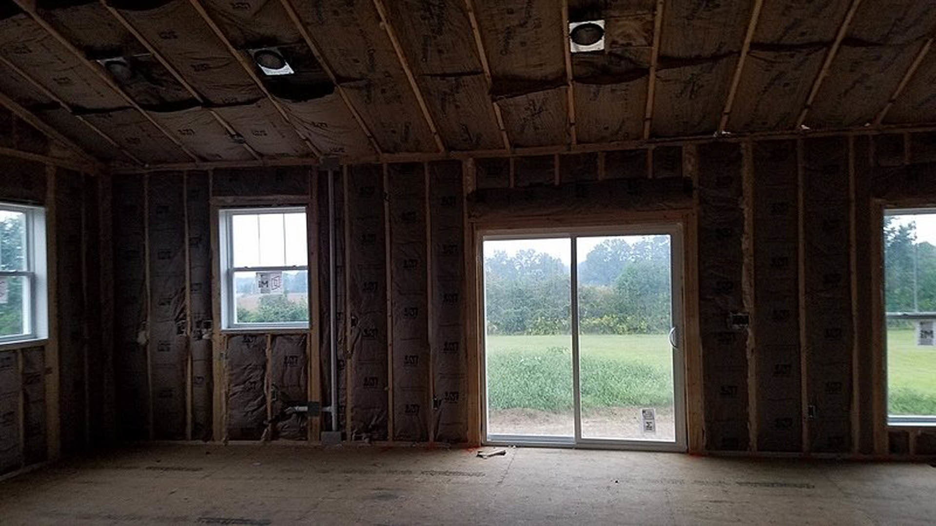 Open room featuring a large window and glass door, wooden plank ceiling with exposed beams, natural daylight illuminating light-colored flooring, window offering view of grassy
