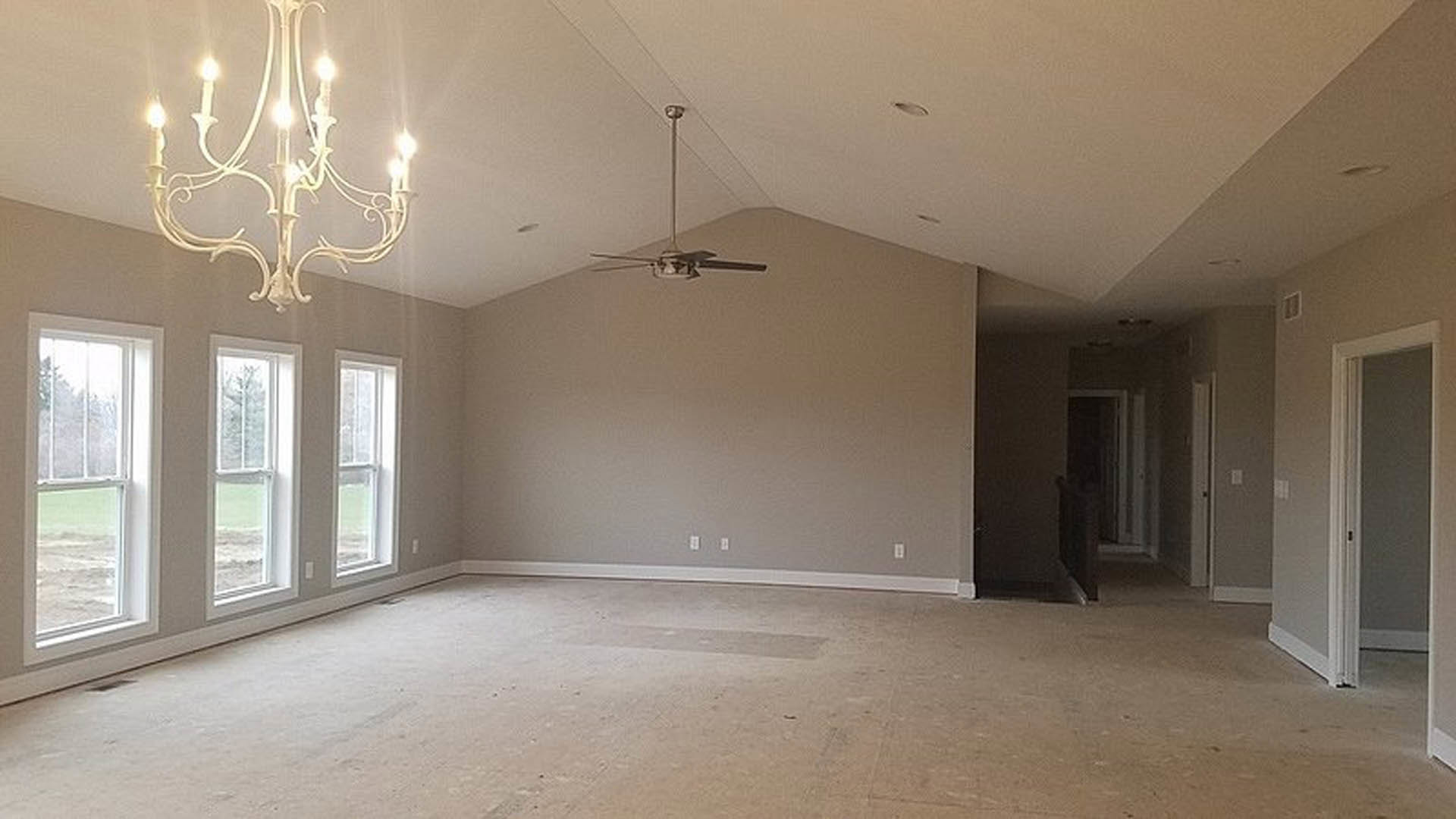 Spacious room with light-colored flooring, multiple windows overlooking grassy yard, white plaster walls, ceiling fan with light fixture, and decorative molding.