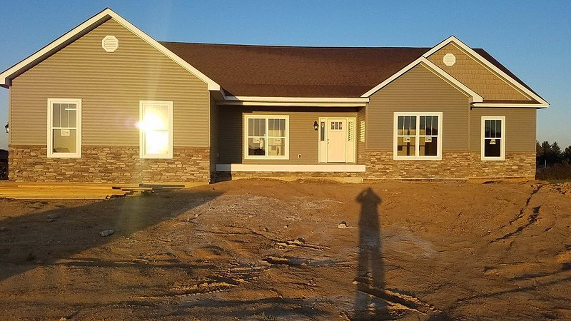 White octagonal house with black trim, prominent front door, white-framed windows, sunlight casting strong shadow across exterior siding