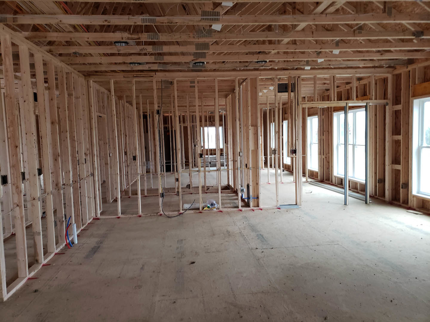 Exposed wood ceiling beams, large window with sunlight, unfinished concrete floor, visible electrical wiring, residential interior under construction