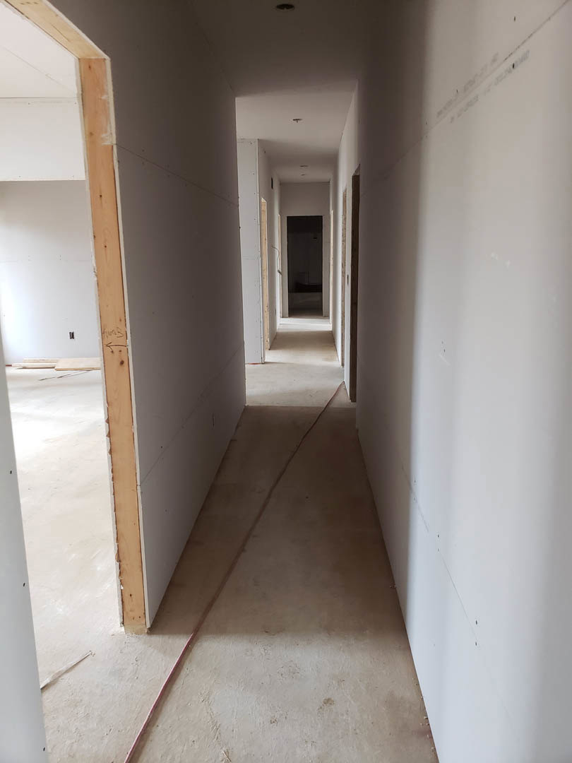 Hallway with smooth white plaster walls, light-colored flooring, black door with white frame, red wire along one wall, soft shadows, multiple doorways