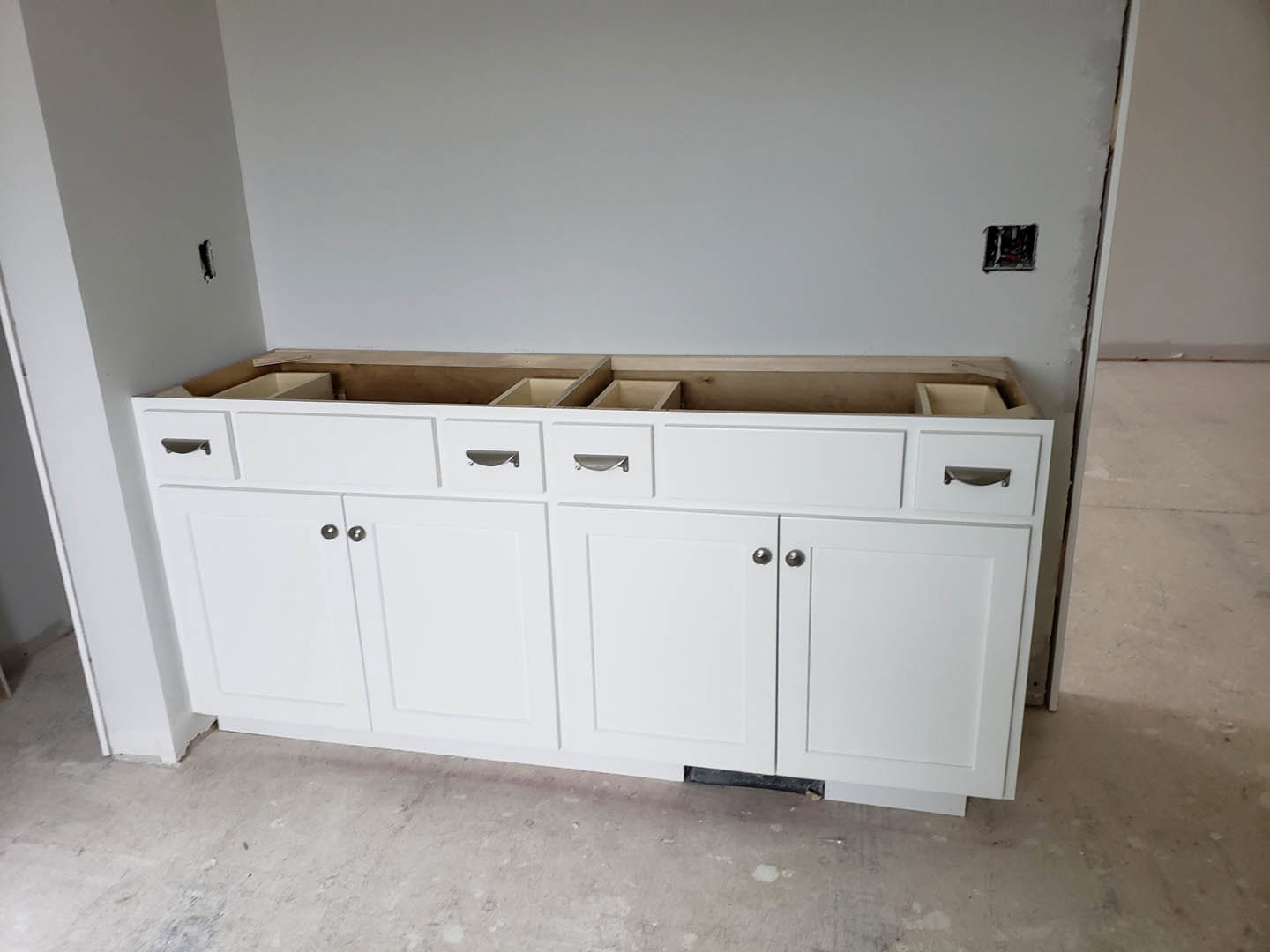 White shaker-style kitchen cabinets with silver knobs, white quartz countertops, and matching backsplash in a bright room with light wood flooring.