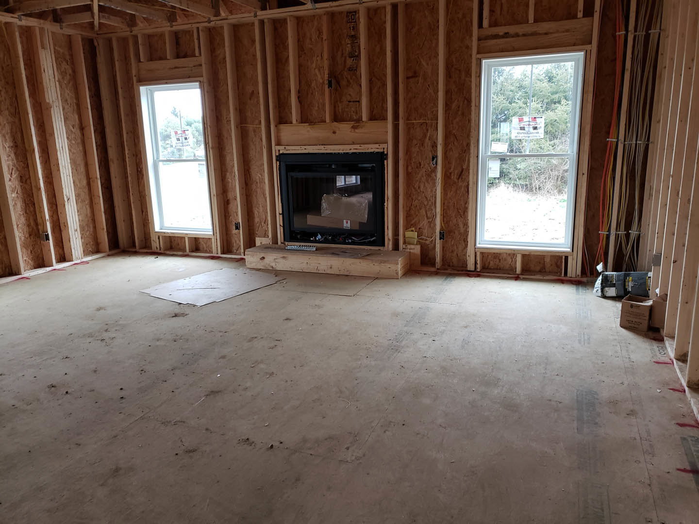 Living room with concrete floor, wood plank step, modern fireplace, exposed ceiling beams, large glass door, and window displaying a sign.