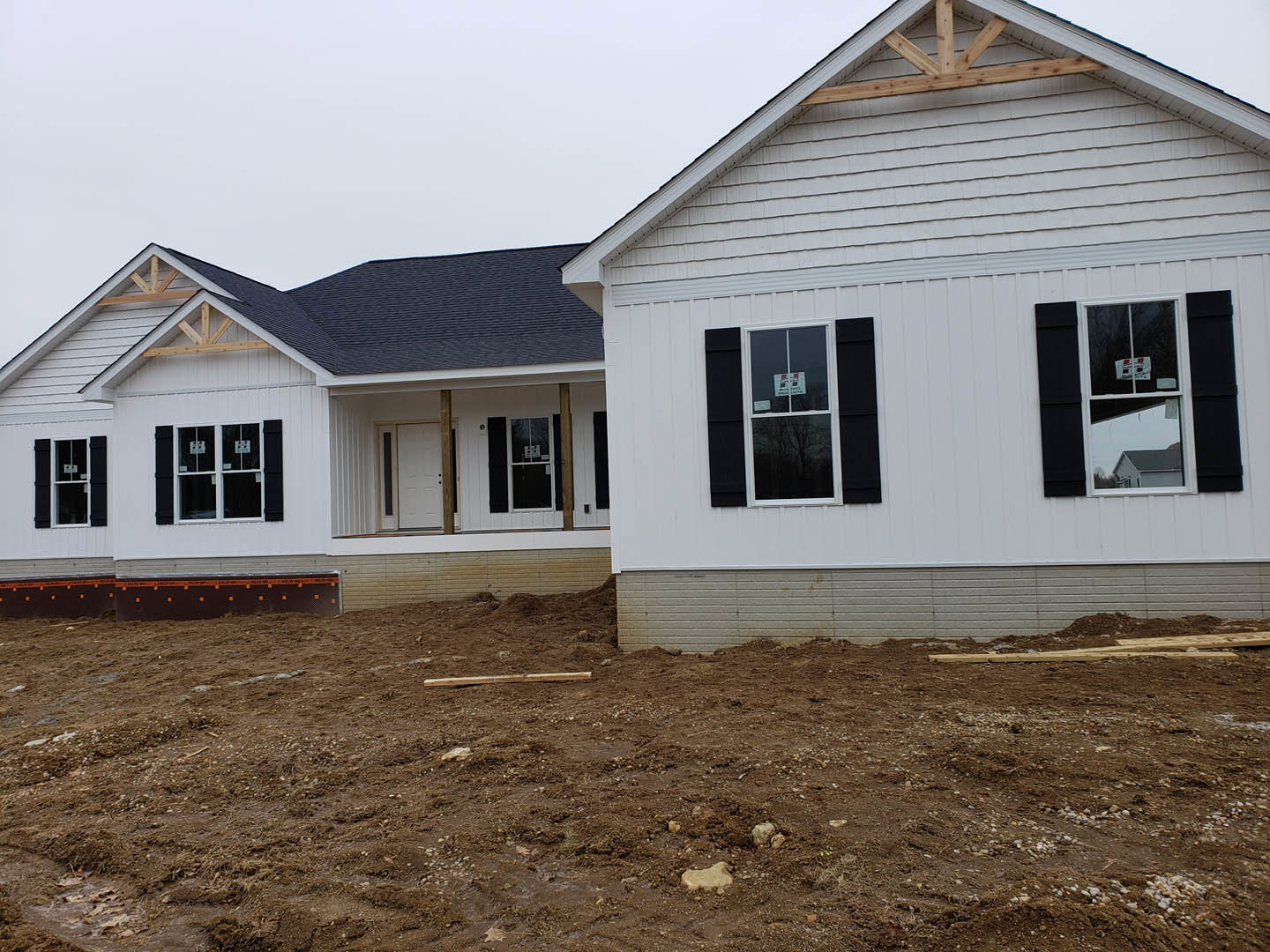 Two-story house under construction with black roof, exposed wooden beams, dirt yard, and window displaying a basketball hoop and construction sign