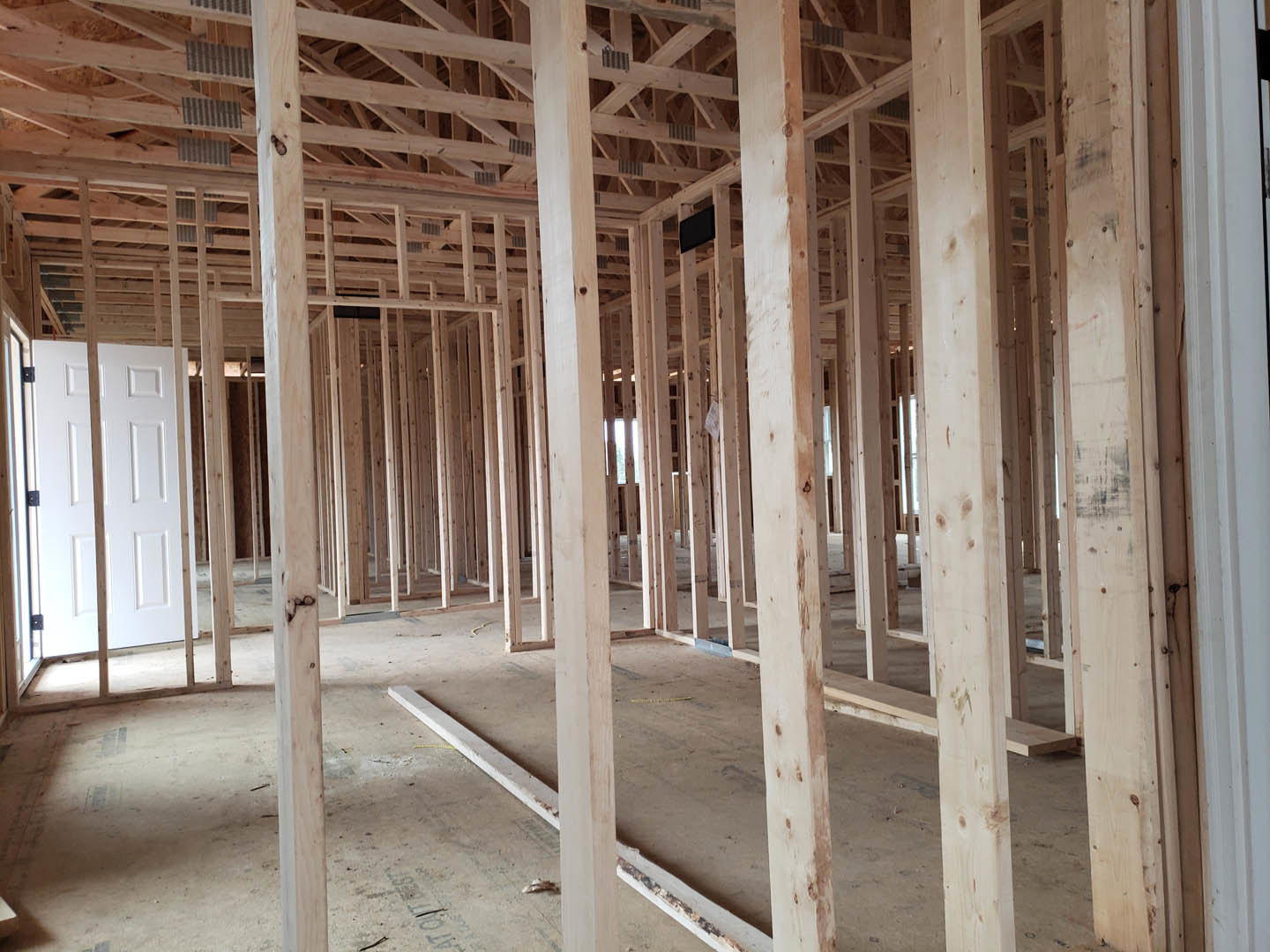 Exposed wooden beams and framing inside a partially constructed home, white door with square panels, unfinished walls, and construction materials visible