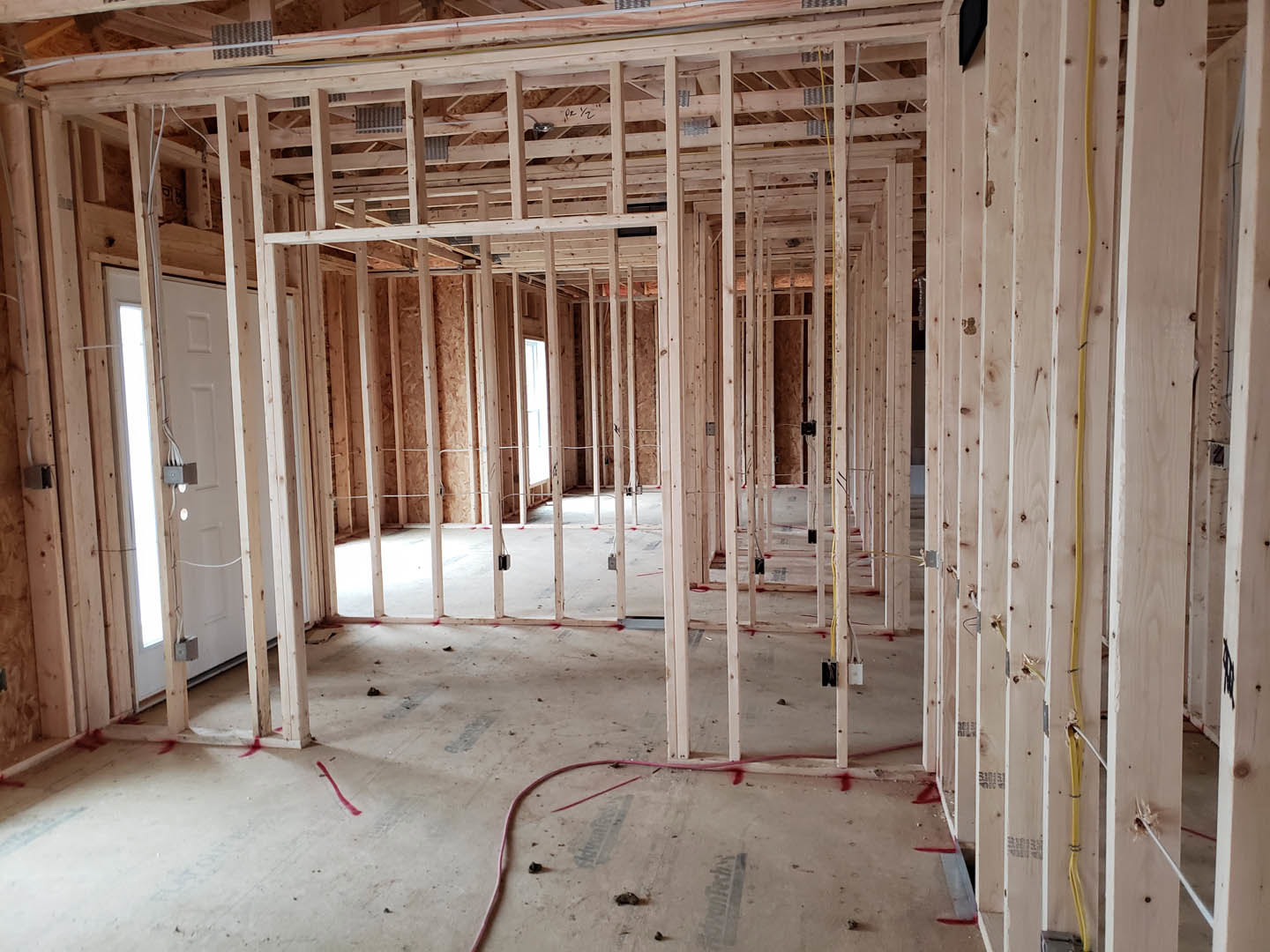 Wood-framed room under construction with exposed beams, unfinished walls, concrete floor, visible wiring box, and plumbing pipe