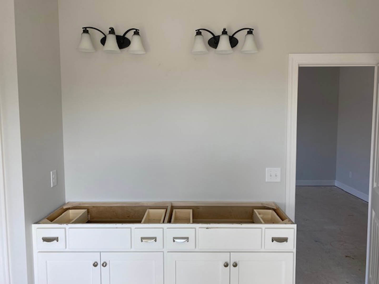 White kitchen with shaker cabinets, black hardware, quartz countertops, bell-shaped pendant light, white wall switch with black buttons, and black cord lamp.