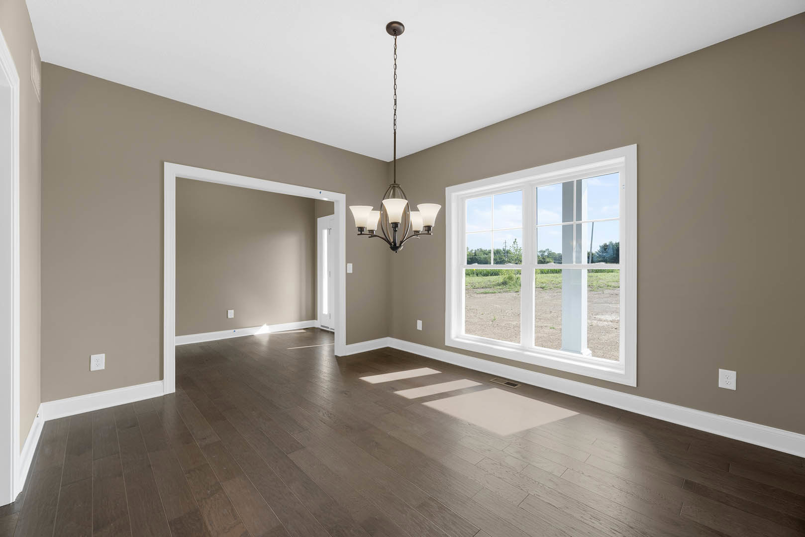 Chandelier hanging from white ceiling above hardwood floor, large windows with field view, floor vent near wall, plaster walls, wood trim