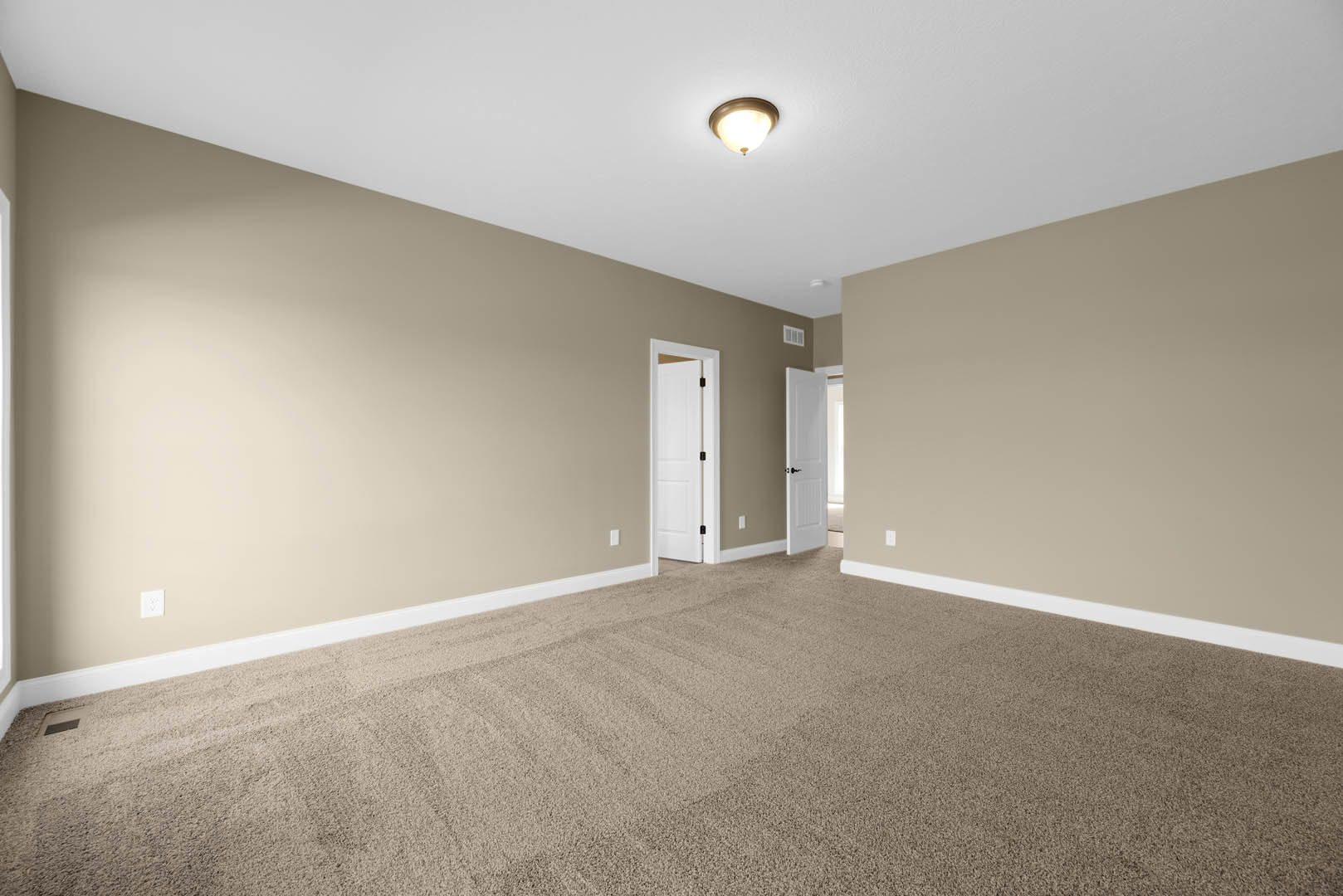 Beige-walled room with white trim, carpeted floor, white door featuring a black handle, and ceiling-mounted light fixture
