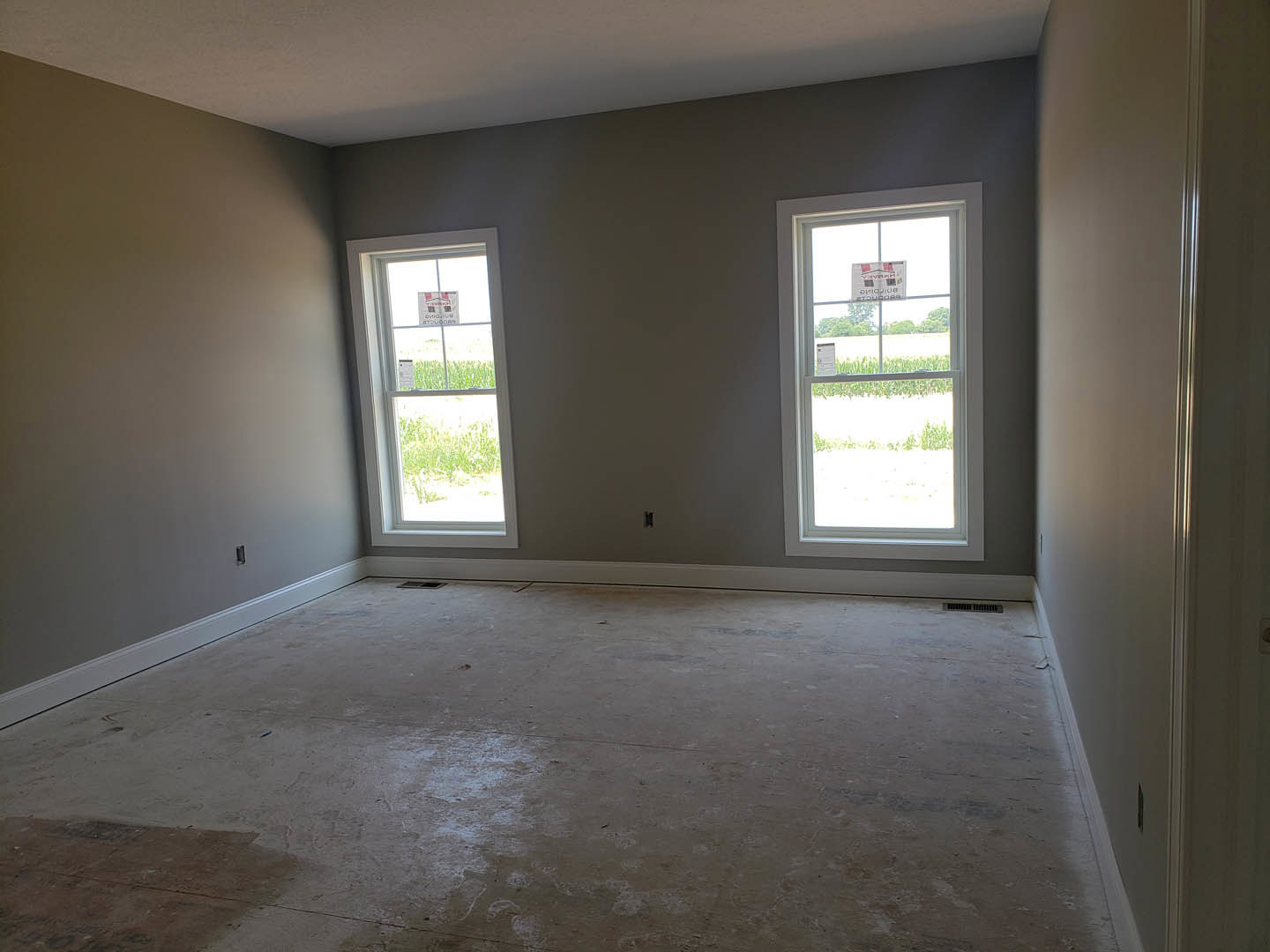 Spacious room featuring two large windows, smooth concrete flooring, and white plaster walls; a window displays a sign with text.
