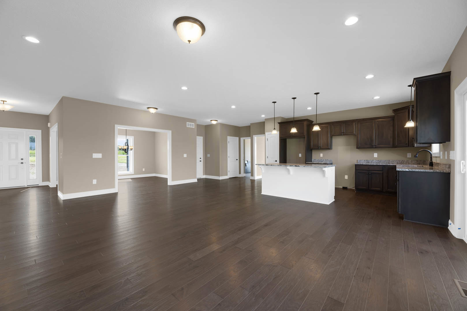 Spacious open floor plan featuring a kitchen with white cabinetry and marble countertops, hardwood flooring throughout, dark accent wall illuminated by ceiling light fixtures, and