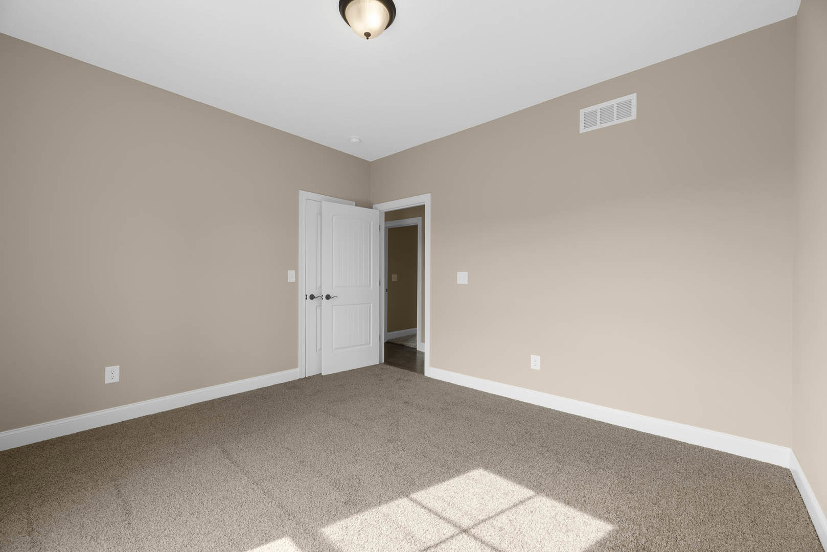 White paneled door with black handles opens into a room with light gray carpet, white walls, ceiling vent, and nearby light switch.