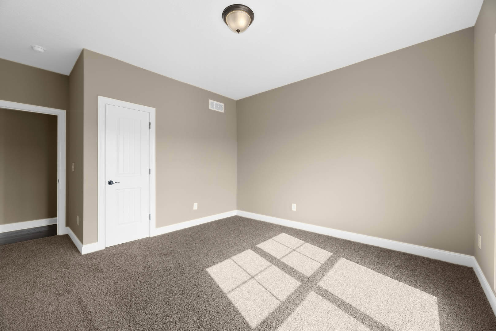 White paneled door with black handle, white door frame, beige carpet flooring, ceiling light fixture, smooth white walls, simple baseboard molding