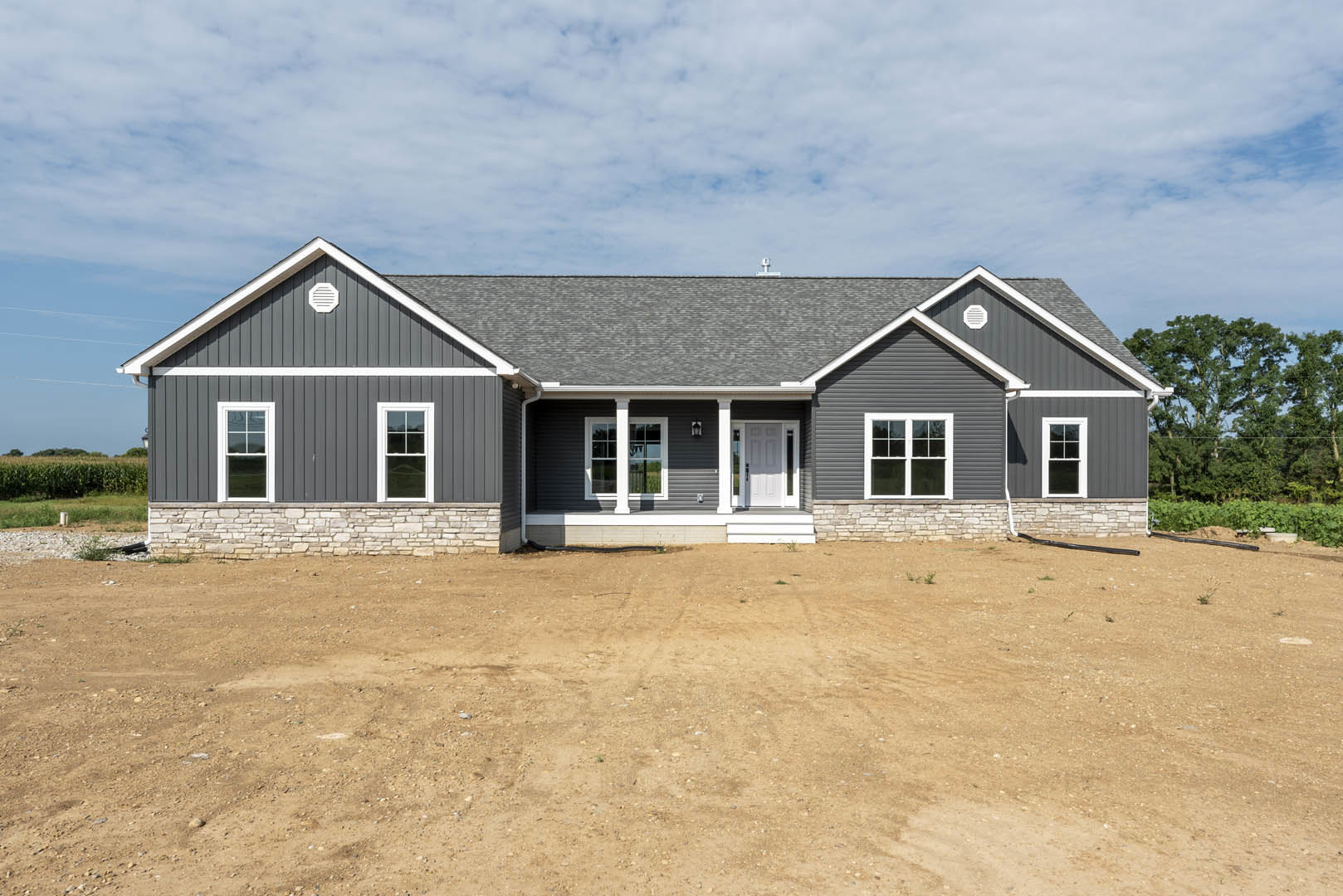 White house with white pillars and window, dirt yard in front, trees in background, cloudy sky overhead
