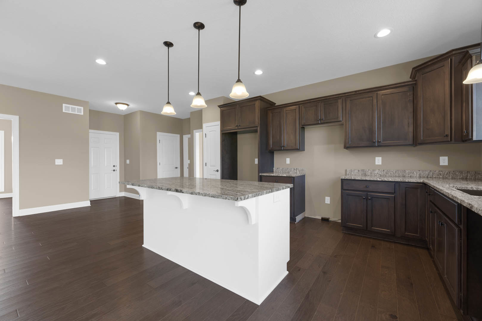 Marble-topped white kitchen island with built-in sink, surrounding white cabinetry, stainless steel appliances, tile backsplash, and pendant light fixtures above