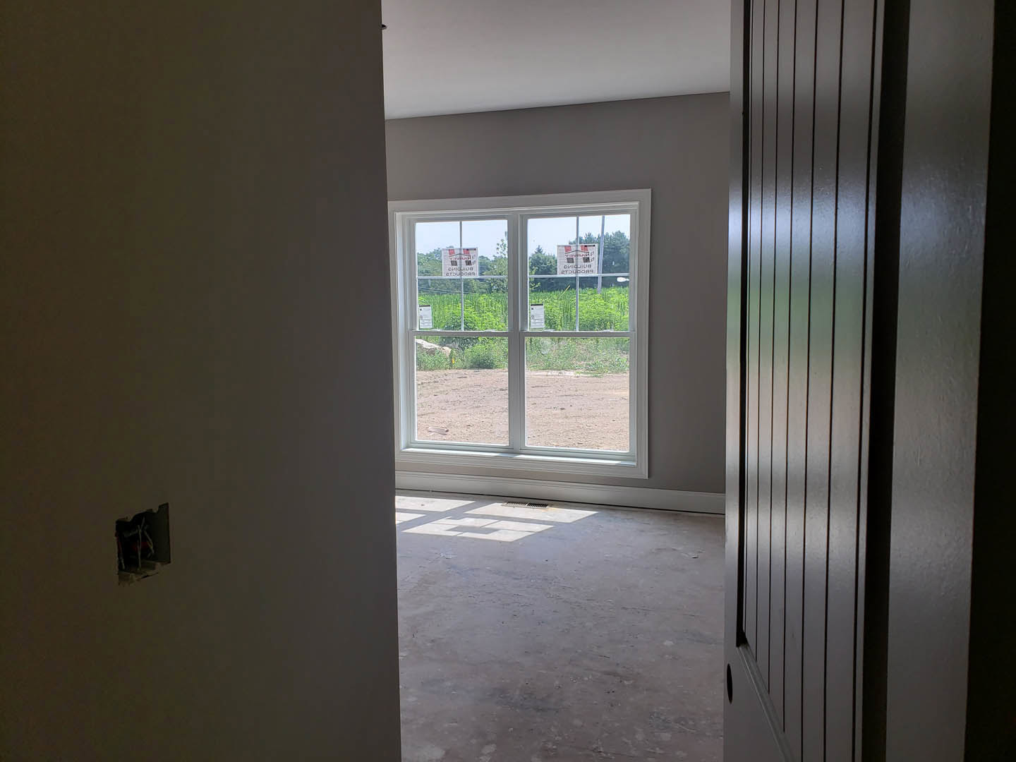 Concrete floor room with white walls, large window displaying signage, and a black-framed door.