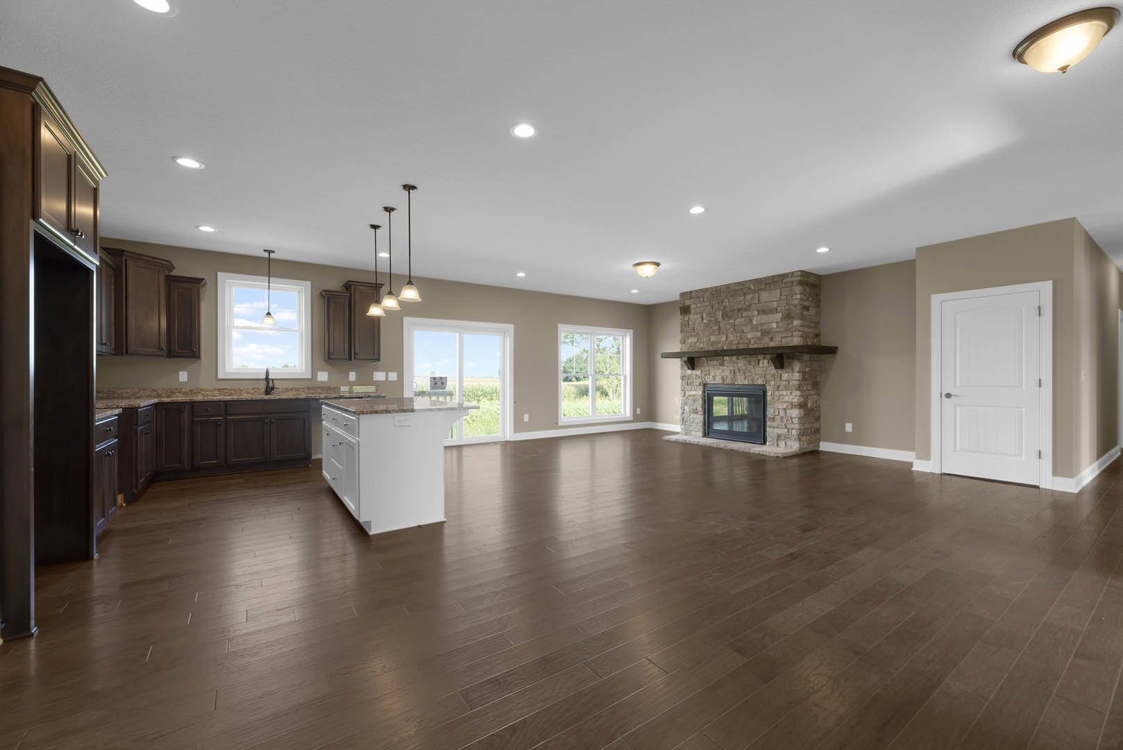 Spacious living room featuring hardwood floors, white kitchen island with marble countertop, glass-door fireplace, white door with silver handle, and large window overlooking the