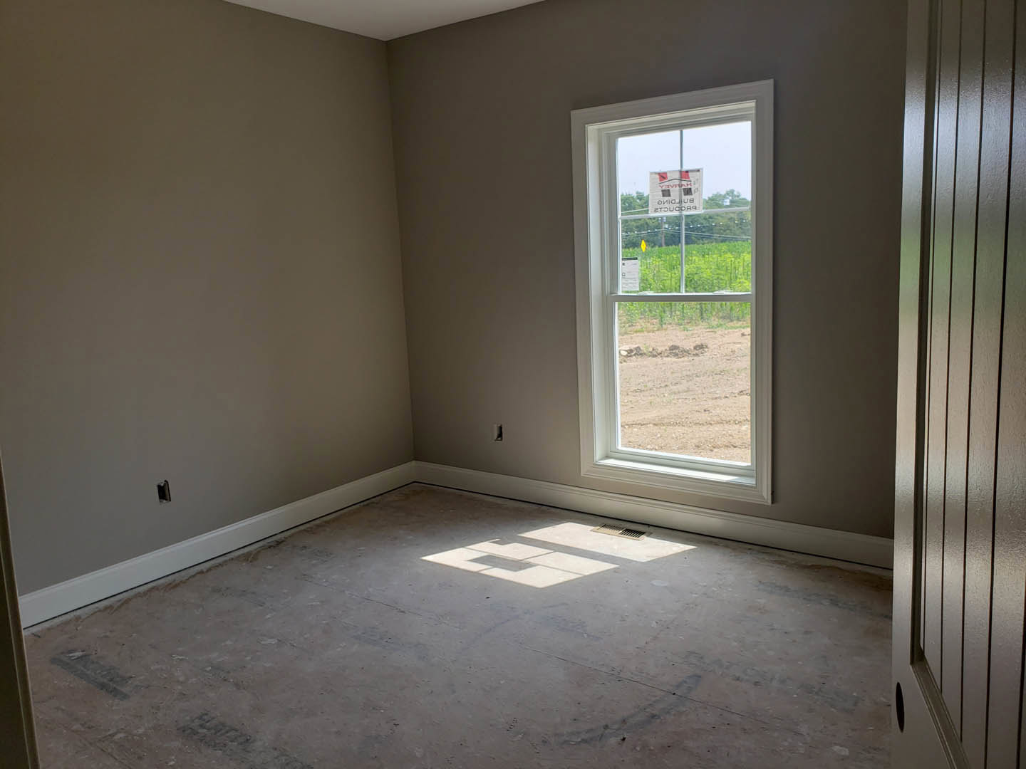 Concrete floor and plaster walls in a room with a large window, daylight streaming in, red and black sign displayed on glass.