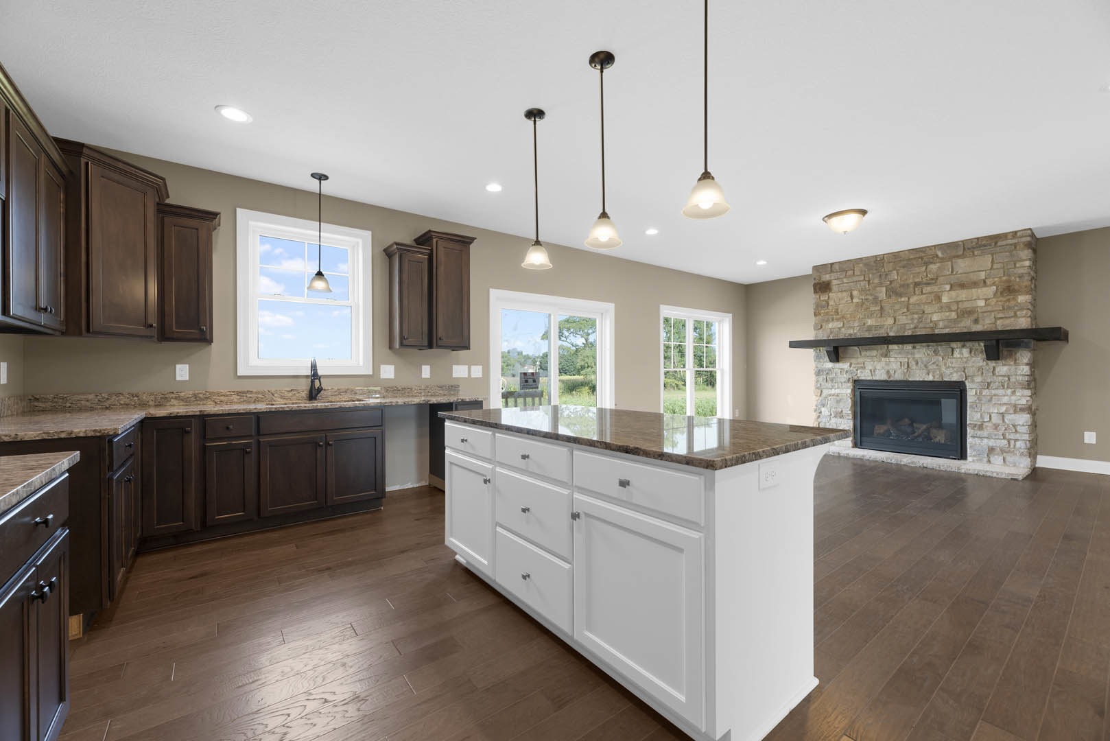 Kitchen with white island featuring drawers, built-in sink, glass-door fireplace, ceiling light fixture, cabinetry, and window overlooking a field