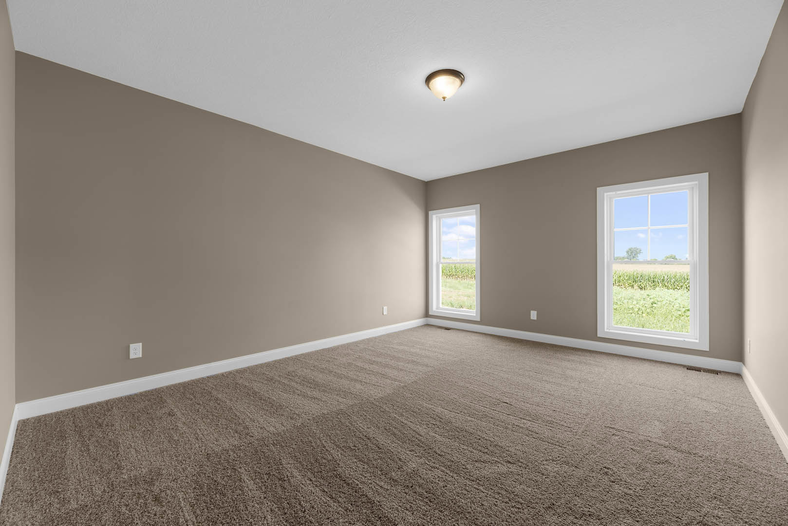 Carpeted room with white walls, ceiling light fixture, large window overlooking cornfield