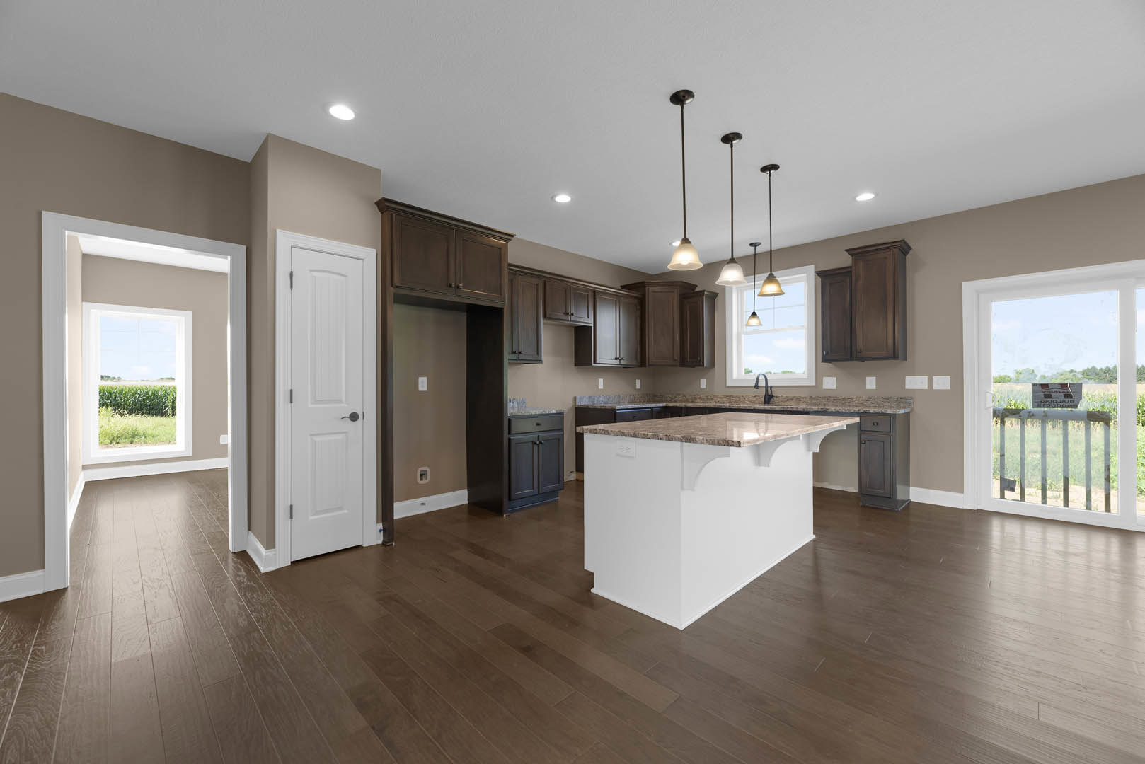 Open kitchen and dining area with light wood floors, white cabinetry, marble-topped island, black hardware, and large window overlooking cornfield