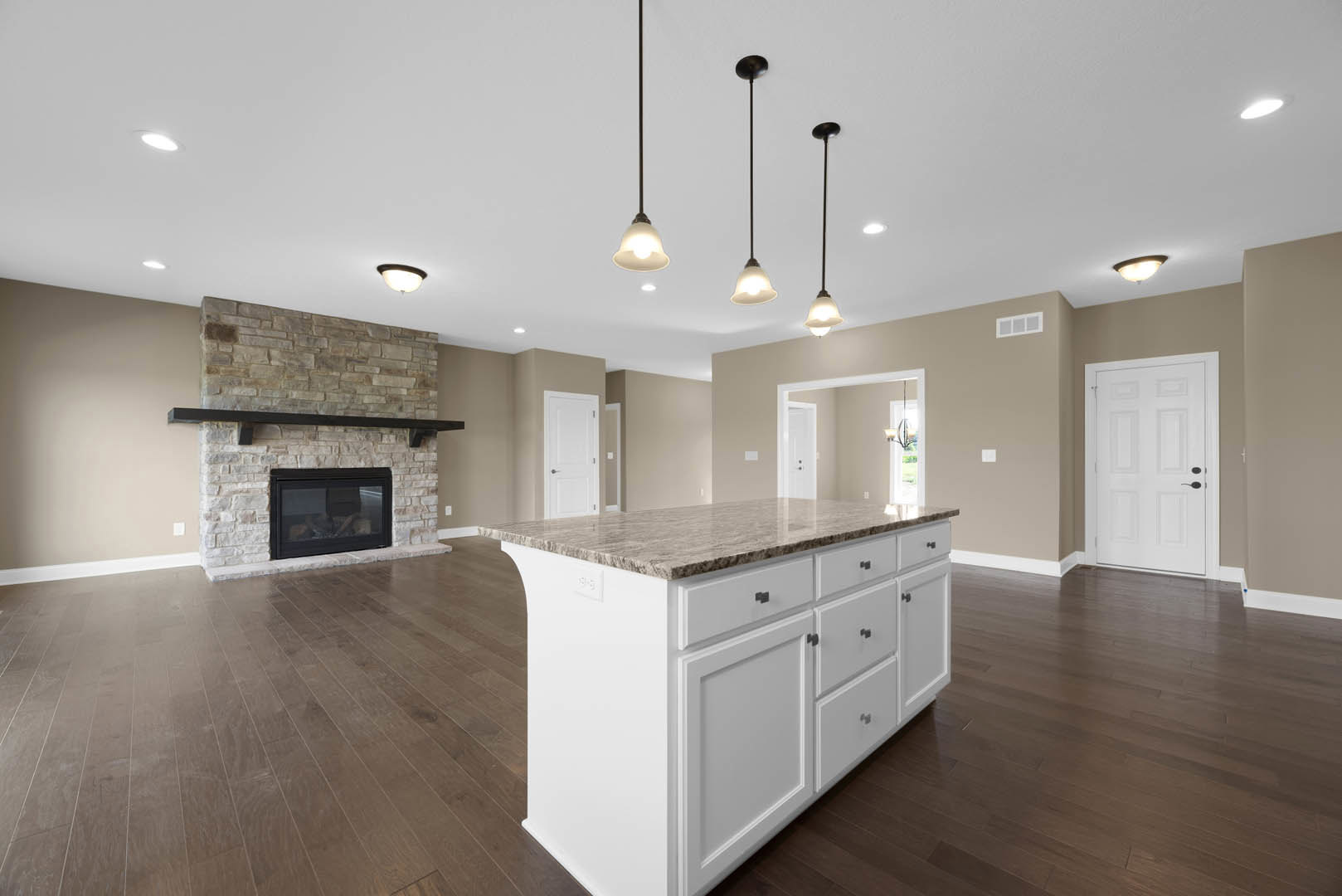 Spacious living room featuring a black glass fireplace, marble kitchen island, white cabinetry with black handles, pendant lighting, and hardwood flooring