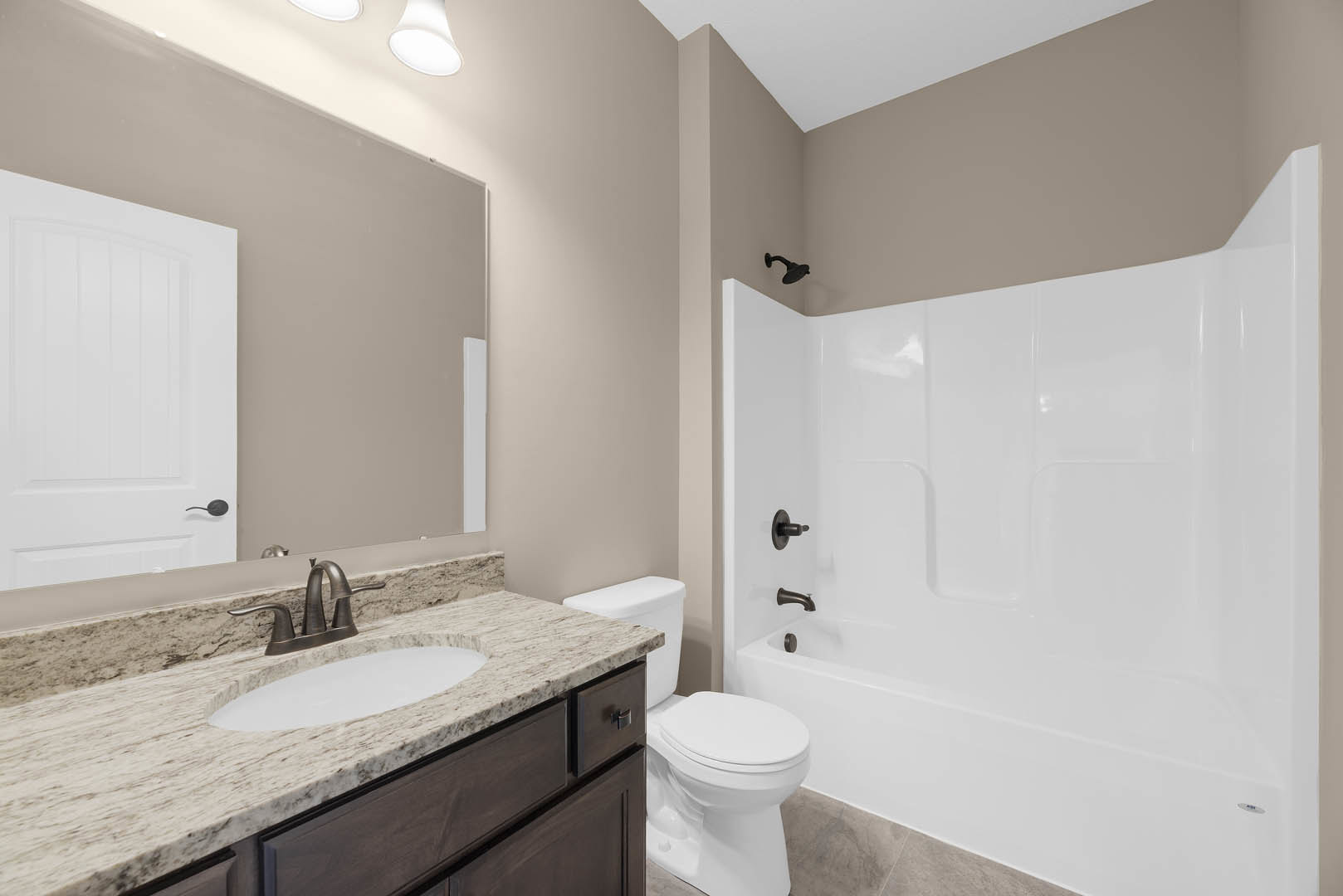 Modern bathroom featuring a white bathtub, tiled walls, sleek countertop with integrated sink, chrome faucet, and adjacent toilet