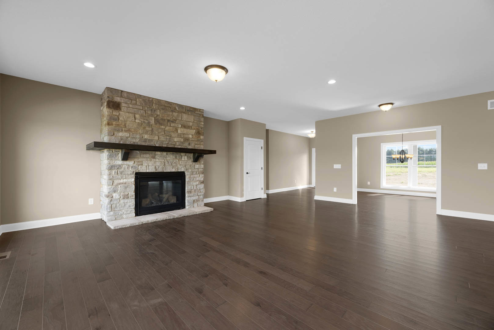 Living room with hardwood floors, central fireplace featuring a glass door and wood mantel, white door with black handle, ceiling light fixture, neutral walls
