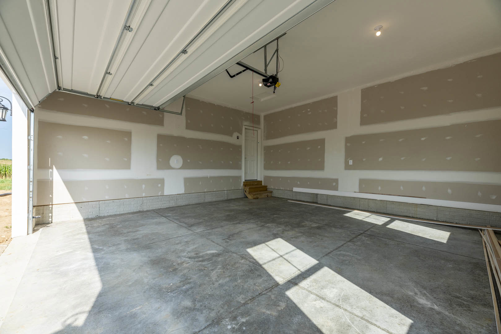 Concrete floor with a white door, wall-mounted light fixture, wooden staircase, and window in a modern interior room.