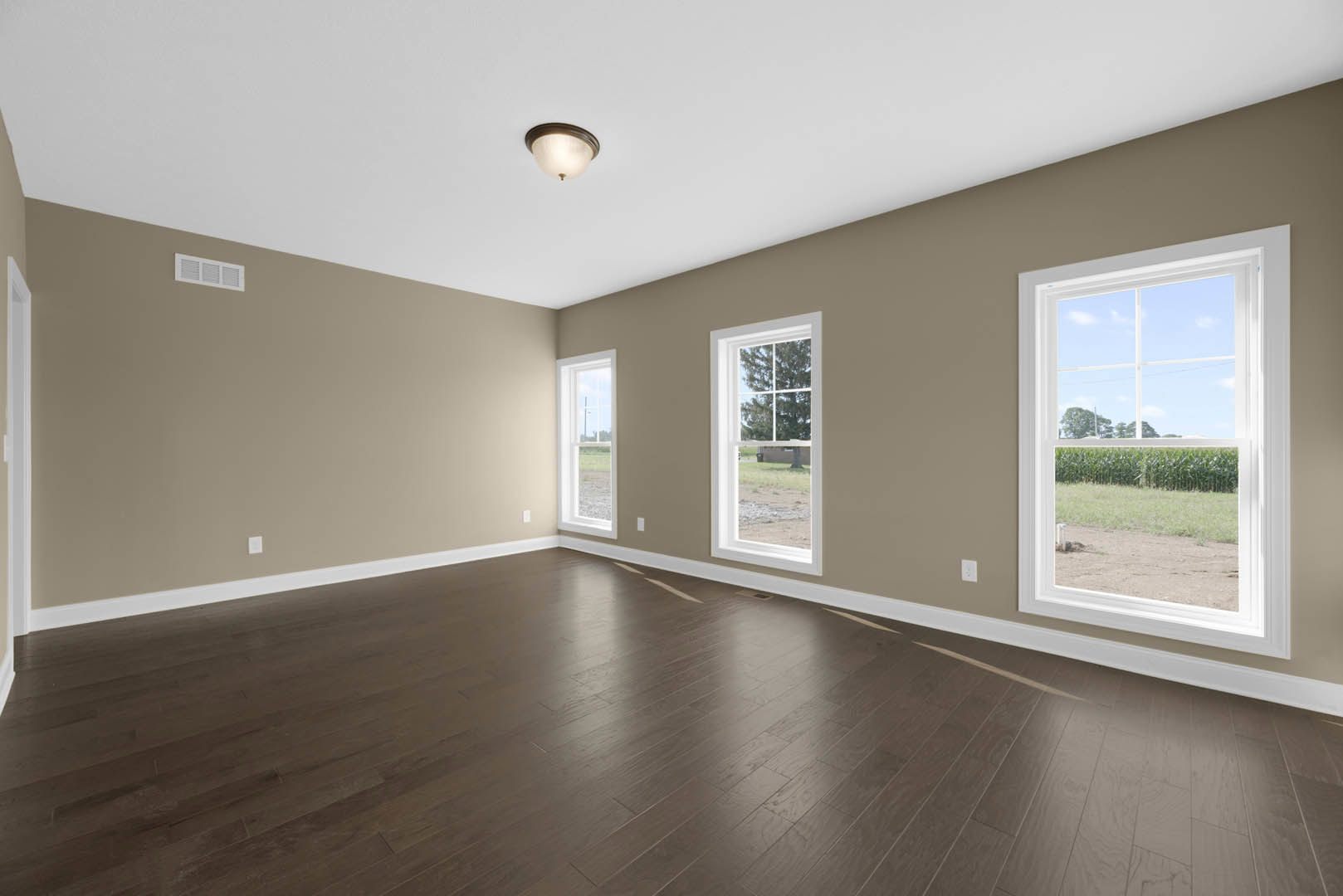 Sunlit room featuring large windows, dark hardwood floors, white plaster walls, crown molding, and a view of a tree and farm outside.