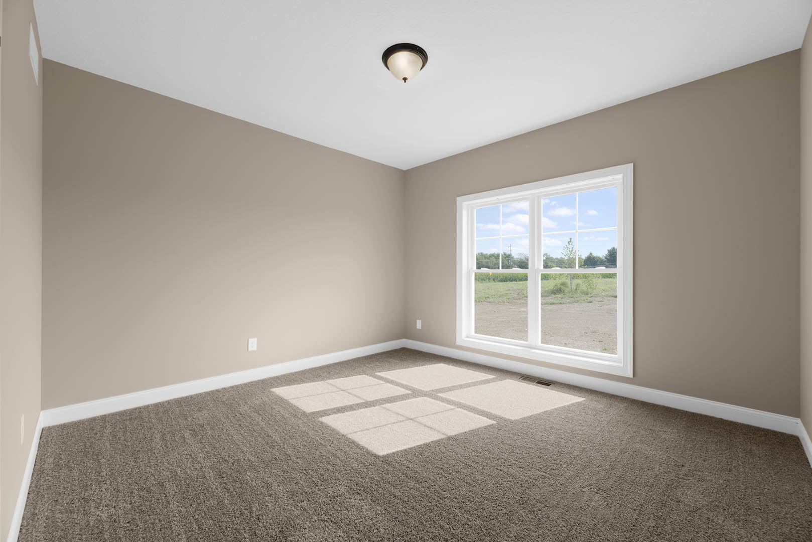 Bright room with square-patterned carpet, large window overlooking grassy field, white walls, ceiling light fixture, and simple molding.