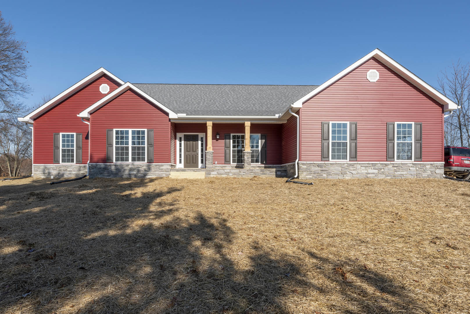 Red siding house with grey roof, white vent, and window, tree shadow cast across green lawn, red van parked nearby.