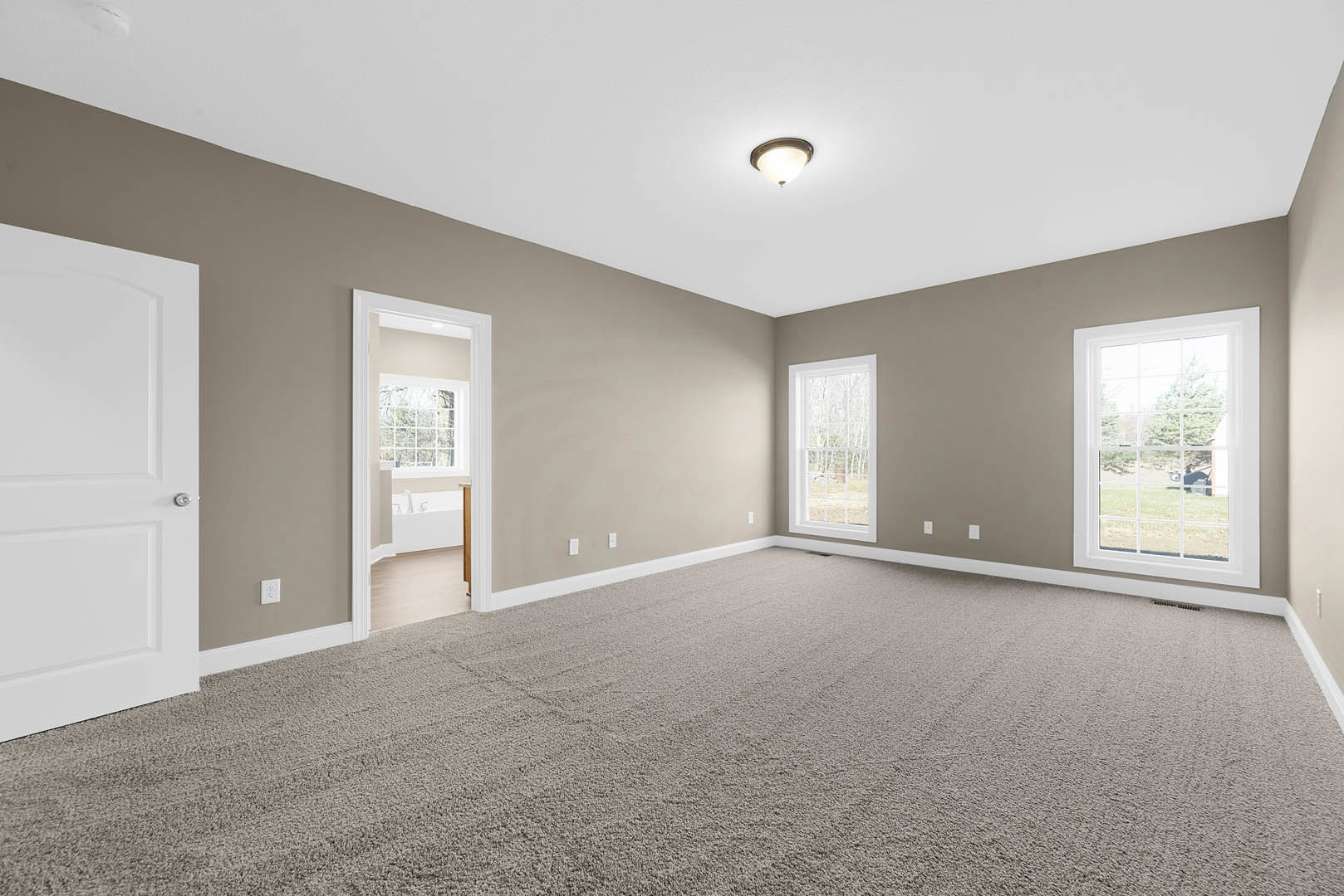 Carpeted room with white door, ceiling light fixture, and large windows overlooking grassy yard and trees